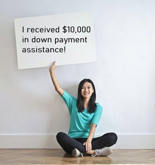 woman-holding-sign-announcing-she-received-$10000-down-payment-assistance-Reazo-real-estate