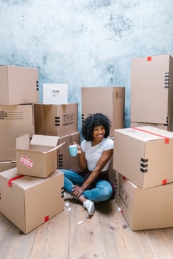 happy-woman-sitting-in-middle-of-moving-boxes-Reazo-real-estate